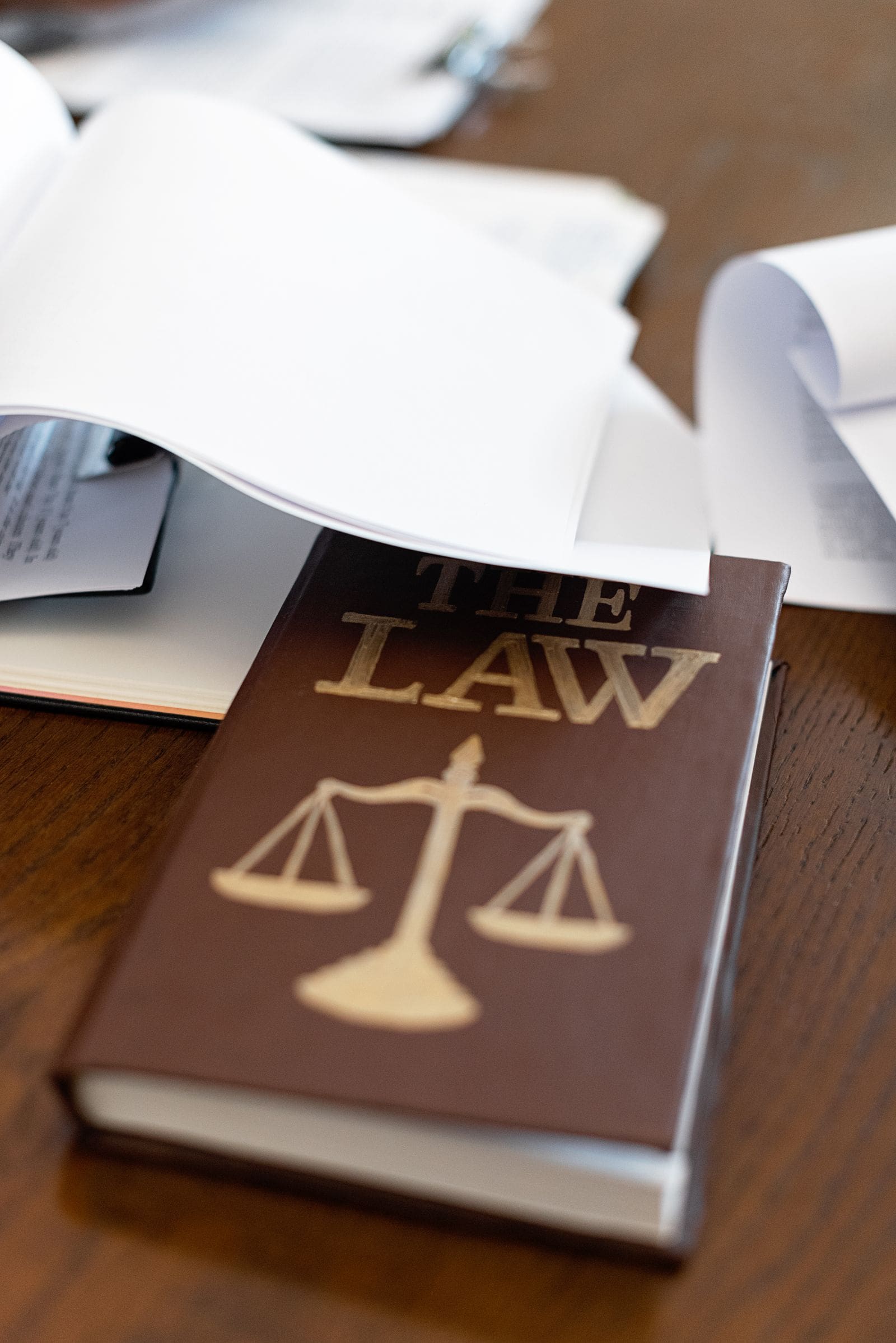 A law book with a scales of justice emblem lying on a wooden desk beside papers